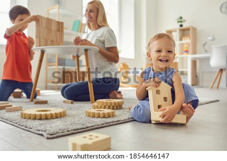Happy family mother and boys children sitting on floor and playing with wooden toy details together at home with room interior at background. Happy childhood and motherhood concept