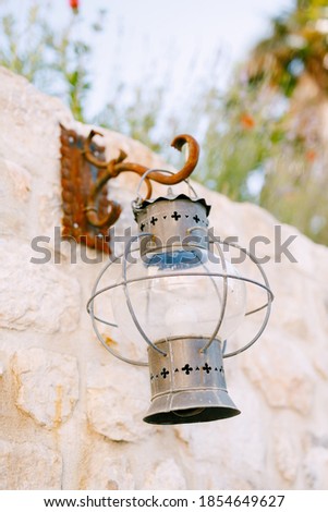 Old metal hanging lantern on a rusty hook on a stone wall.