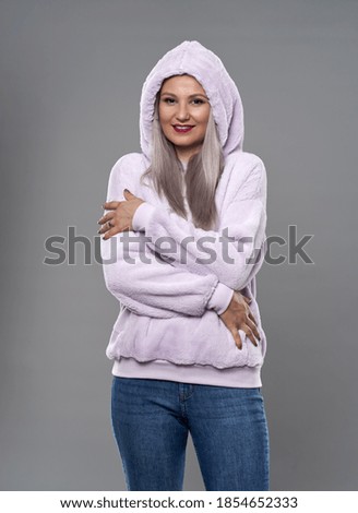 Young woman in a warm hooded pink sweater on gray background