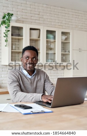 Smiling black business man looking away using laptop computer working from home office. Happy thoughtful african student thinking of inspiration ideas studying on pc sits at kitchen table, vertical.