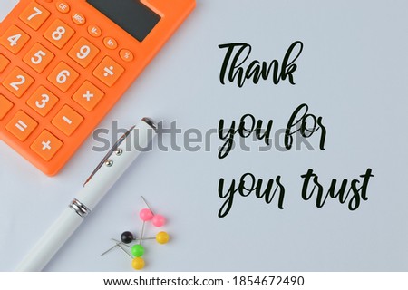 Top view of calculator, pen, pinboards on a white background written with text THANK YOU FOR YOUR TRUST. Business concept. 