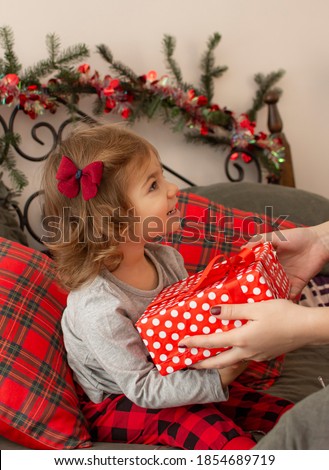 Mother giving excited daughter Christmas present. Cute kid receiving  gift from mommy during new year celebration. Little girl is holding a gift box. Winter holidays lifestyle concept. Happy family.