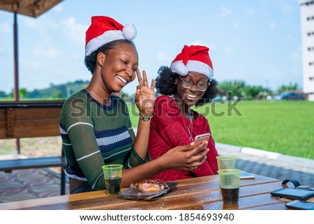 Two beautiful African women celebrating Christmas,holding phone and showing a quality sign-people communicating on internet