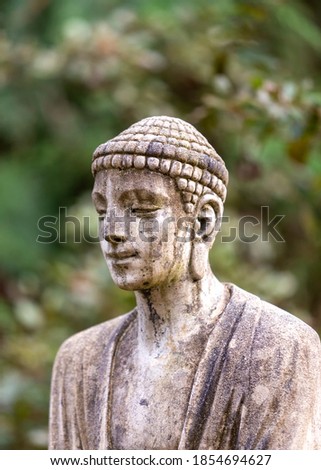 Ancient statue of Buddhist monk in the woods with background bokeh 