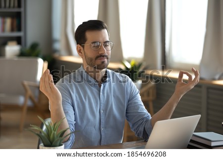 Serene office male employee sit at desk relaxing doing yoga, practice meditation to reduce stress relief fatigue feel internal balance at workplace, improve mindfulness, maintain mental health concept Royalty-Free Stock Photo #1854696208
