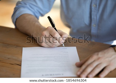 Man sit at table hold pen put signature on lawful agreement paper, subscribing name surname in statement with legal value. Hired employee signing contract agree terms and conditions, good deal concept