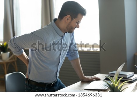 Businessman touches lower back feeling pain sudden ache while get up out of office chair, muscular spasm, strain caused by sedentary lifestyle, prolonged inactivity, sit in incorrect posture concept Royalty-Free Stock Photo #1854696331