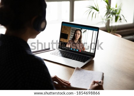 Back view concentrated young woman in headphones involved in online education class, listening to skilled lecturer, studying foreign language remotely, gaining professional knowledge, writing notes. Royalty-Free Stock Photo #1854698866