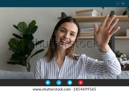 Head shot relaxed smiling young woman sitting on sofa waving hand in hello gesture, greeting friends or family at online video call distant conversation, computer software application display view. Royalty-Free Stock Photo #1854699565