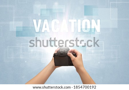 Close-up of a hand holding digital camera with VACATION inscription, traveling concept