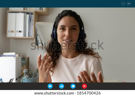 Head shot computer display view beautiful caucasian businesswoman in headphones talking holding video web camera call with colleagues, enjoying online meeting, working learning distantly from home. Royalty-Free Stock Photo #1854700426