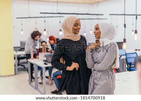 Portrait of two African American businesswomen talking to each other while standing in a modern business office with their colleagues. Marketing concept. Multi-ethnic society.