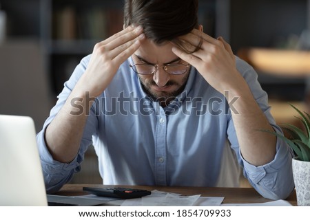 35s businessman sitting at workplace desk with bowed head, on table lot of unpaid receipts, overdue bills. Concept of small business owner bankruptcy, financial problems and crisis, money overspend Royalty-Free Stock Photo #1854709933