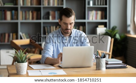 Focused business man sit at workplace desk at home office cozy room working on laptop, make analysis sales stats results, learn graphs and making financial forecasts. Busy workday, modern tech concept Royalty-Free Stock Photo #1854710251