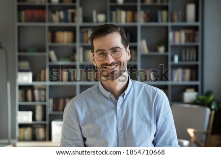 Head shot handsome millennial 30s professional employee worker posing for camera at modern office. Business portrait, creative occupation person. Teacher, experienced business coach indoors concept Royalty-Free Stock Photo #1854710668