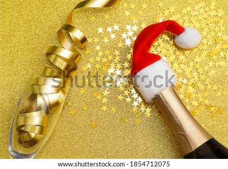 santa claus hat and bottle of champagne.santa  one vine glasses with golden ribbon on yellow background. place for text, close-up image. top view. happy new year and merry christmas
