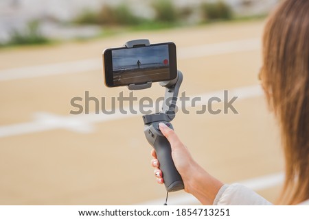 Woman hand holding gimbal with phone. Taking pictures and live video near the ocean. Vlog and video blogging concept. Royalty-Free Stock Photo #1854713251