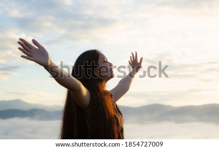 Worship God concept: Happy girl raised hand on blurred mountain sunrise background. Ai Yerweng, Bethong, Yala, Thailand, Asia