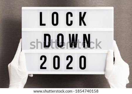Hands in white gloves hold Light box with message lockdown 2020. Word of the Year 2020 is lockdown. Social media content.
