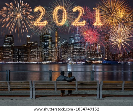 2021 written with Sparkle firework with multicolor of fireworks on back side couple sitting and looking New york Cityscape background, USA downtown skyline,Happy new year and merry Christmas concept