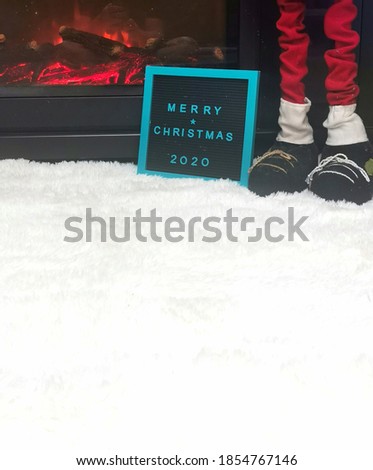 Merry Christmas spelled on a letter board in front of an electronic fireplace with Santa standing by.  