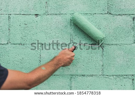 Green teal paint roller on brick wall