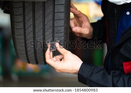 Mechanic checking checking the depth of car tire tread.  Car maintenance and auto service garage concept. Royalty-Free Stock Photo #1854800983