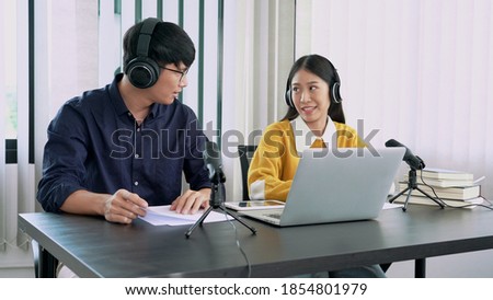 Asian woman radio hosts gesturing to microphone while interviewing a man guest in radio station during a show for radio live in the Studio
