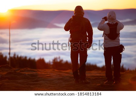 Couple of young man taking picture of sun rise at mountain peak above the clouds. temperature inversion atmospheric property