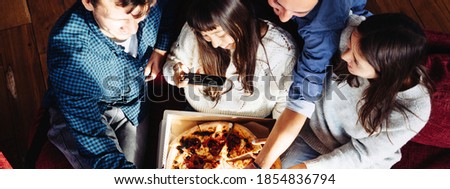 Group of happy friends at home party. Eating pizza together. Asian woman taking picture of the the slice to share memory. Top view