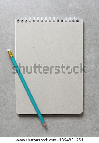 A spring notebook with a sheet of craft paper A5 with simple green graphite pencil on light grey concrete background. Concept of new idea, business plan and strategy, development and implementation of