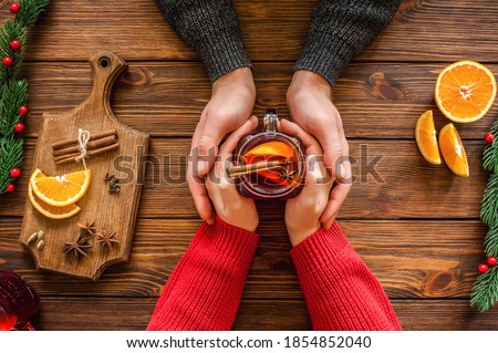 Womans and mens hands holding hot  glass mug. Christmas hot drink - mulled red wine with spices and fruits in the hands of men and women. New Year decoration on a wooden background. Top view Royalty-Free Stock Photo #1854852040