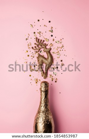 Shiny golden champagne bottle with explosion made of deer and golden confetti stars. Glamour Christmas or New Year celebration concept. Trendy party holiday background.