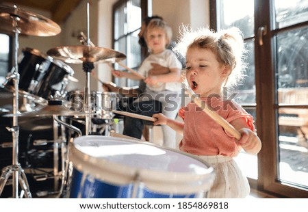 Portrait of small girl indoors at home, playing drums. Royalty-Free Stock Photo #1854869818