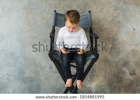 little boy with dark hair sitting on a high chair and watching a cartoon