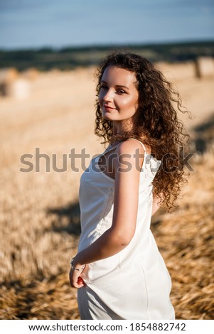 Portrait of a young curly woman in a wheat field, where the wheat is mown and the sheaves are standing, enjoying nature. Nature. sun rays Agriculture