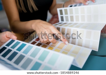 Close-up of two women choosing samples of wall paint. Interior designer consulting a client looking at a color swatch. House renovation concept Royalty-Free Stock Photo #1854889246