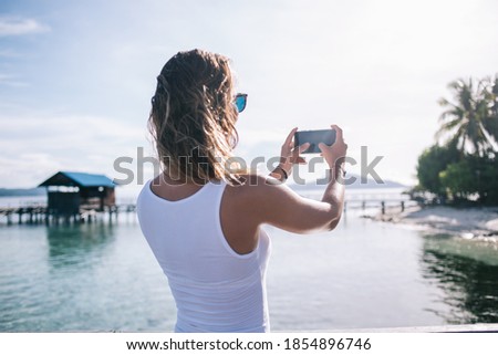 Female blogger with modern mobile gadget focus camera clarity for making good content images during getaway travelling for visiting Hawaii Environment, millennial woman shooting live streams video