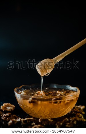 Wooden honey spoon dipped in a jar full of honey and nuts placed on a black background. Honey dripping around, pleasing and inviting photos.
