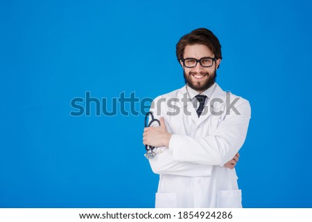 A young bearded doctor on a blue background in a white coat looks at the camera. COVID-19. Self isolation. Stay home concept. Quarantine. Banner. Place for text