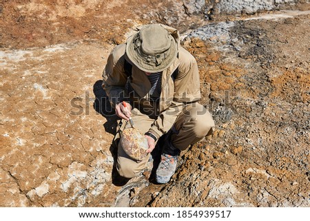 paleontologist holding and brushes a rounded ovoid fossil resembling an dinosaur egg in a desert  Royalty-Free Stock Photo #1854939517