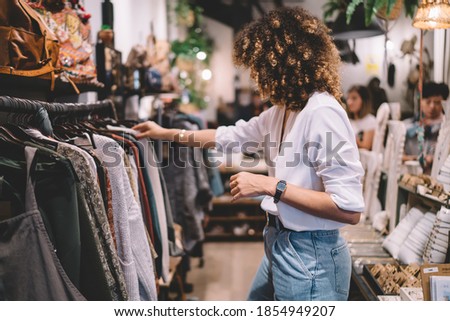 Caucaisan female customer with curly hair buying clothes in boutique using fitting concept while choosing, professional stylist creating trendy look concentrated on selection in designer shop Royalty-Free Stock Photo #1854949207