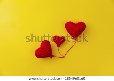 three knitted red heart-shaped balloons in row on yellow background, concept of love and family