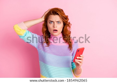 Photo portrait of shocked upset woman holding head phone in one hand isolated on pastel pink colored background