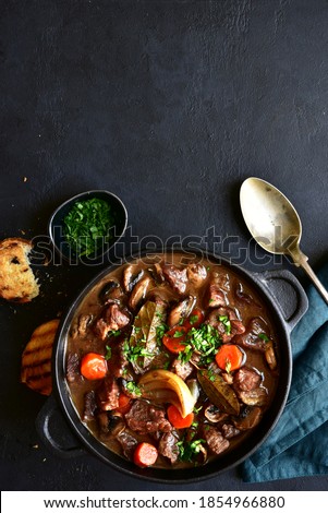 Beef bourguignon - meat stew with vegetables and mushrooms with red wine in a skillet over black slate, stone or concrete background , traditinal dish of french cuisine. Top view with copy space. Royalty-Free Stock Photo #1854966880