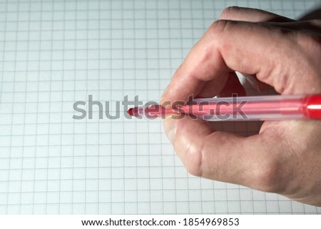 A hand of white caucasian man with a pink pencil is writing on a checkered notebook. Copy space.
