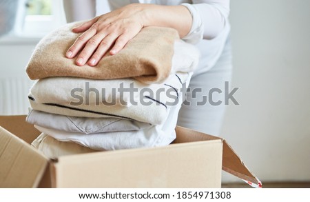 Woman packs clothes for a clothes donation in a box or tidies up Royalty-Free Stock Photo #1854971308