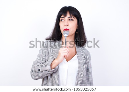Very hungry European young business woman wearing checkered suit over isolated white background holding spoon into mouth dream of tasty meal
