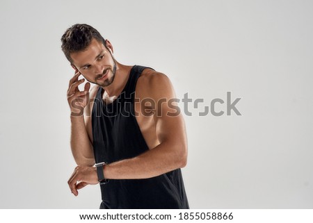 Fitness app. Young handsome caucasian athlete with smart clock and earphones looking to side while standing on gray background. Sport, workout, training and technology concept