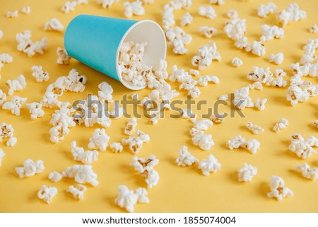Popcorn in a blue paper cup scattered on a yellow background. Minimalist concept. Top view. Copy, empty space for text